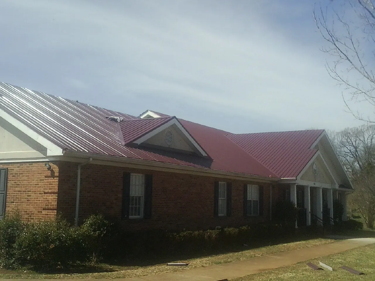 Red metal roof with gabled entries on a long brick building, from a Hail Damage Roof Repair job in Garwin