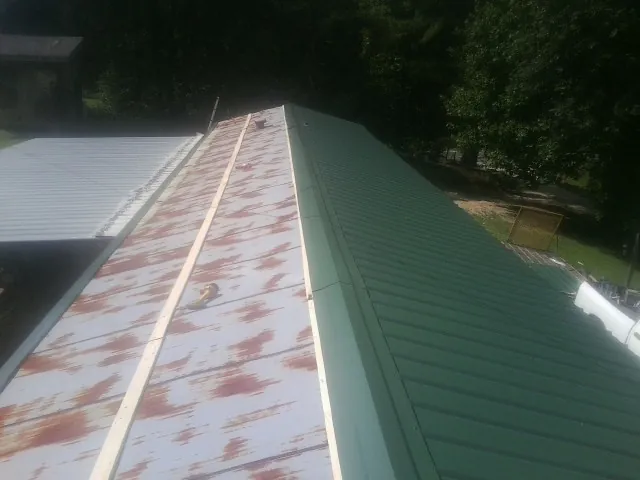 Old rusted panels beside newly installed green metal roofing — Wind Damage Roof Repair by Roofing Brothers in Garwin