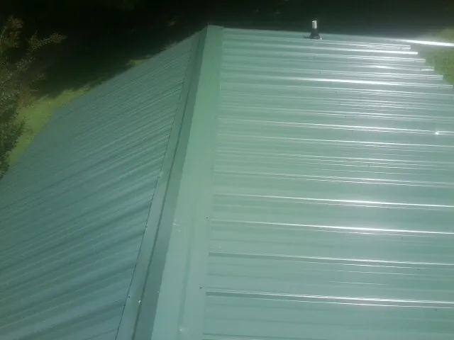 New green metal panels meeting at the ridge of a roof — Flat Roof Repair work by our crew in Garwin