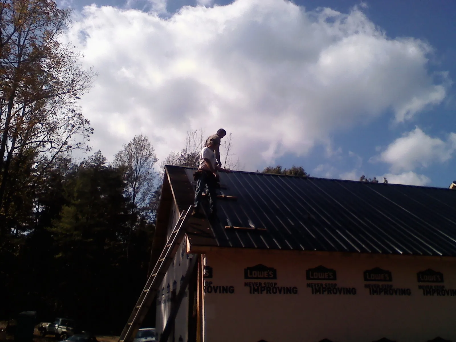 Roofer fastening dark metal panels high against a cloudy sky, from a Roof Inspection job in Garwin